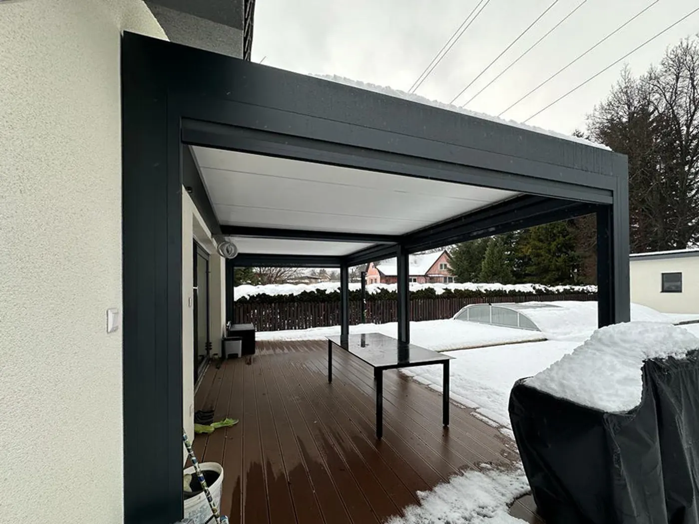Pergola bioclimatique adossée aux lames blanches, jardin enneigé