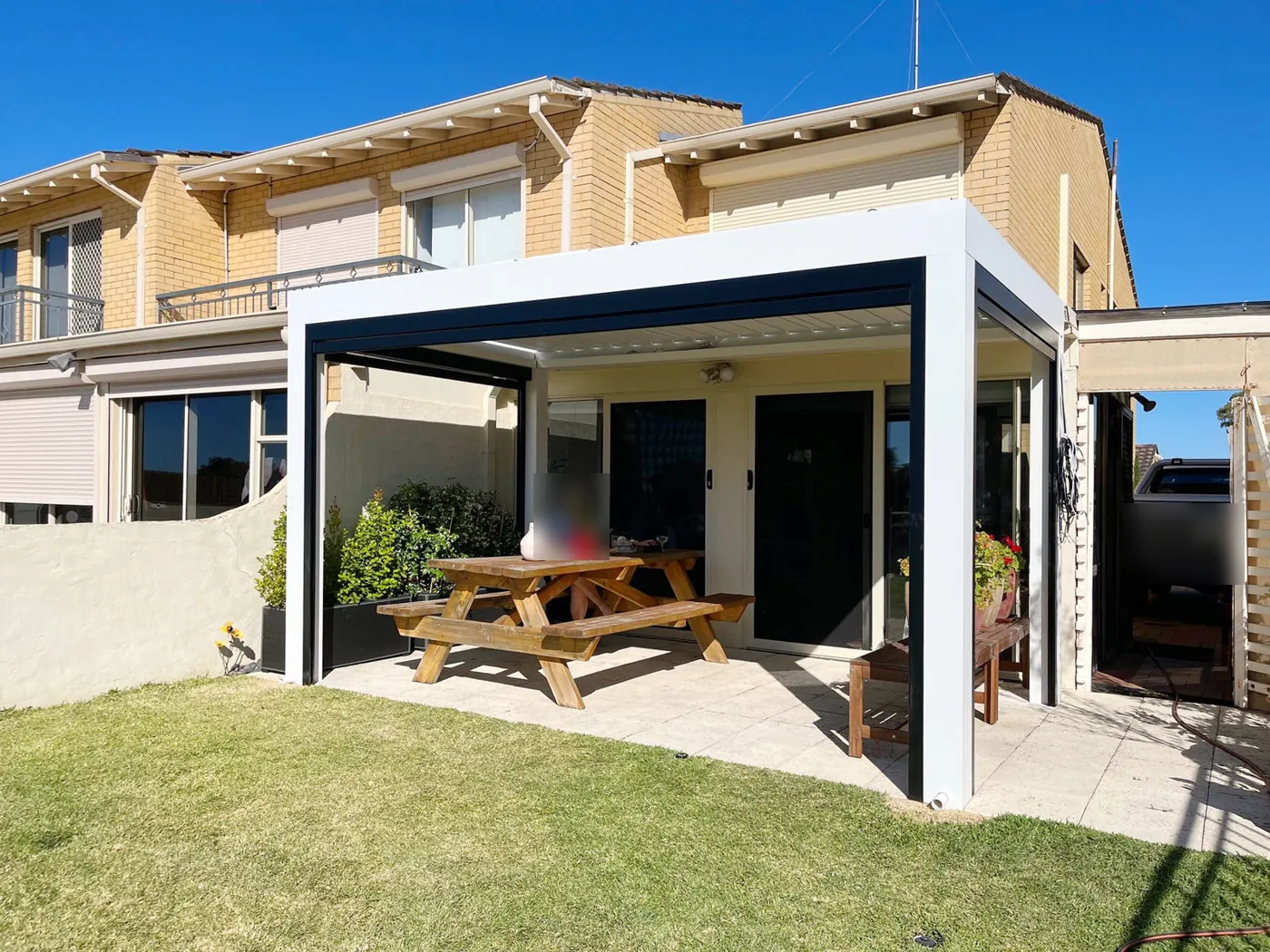 Pergola bioclimatique blanche abritant une table de pique-nique