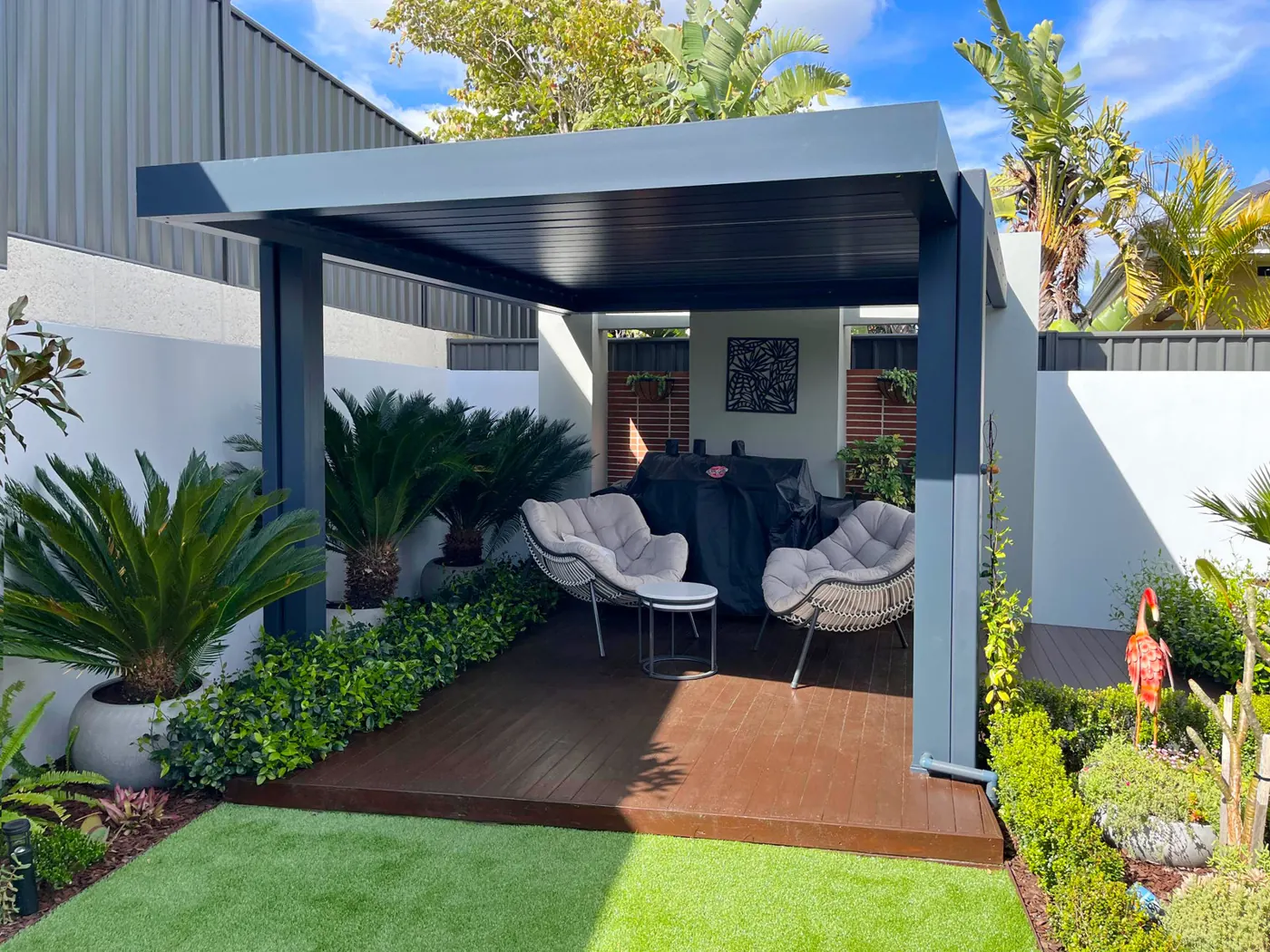 Pergola bioclimatique abritant deux fauteuils dans un jardin tropical